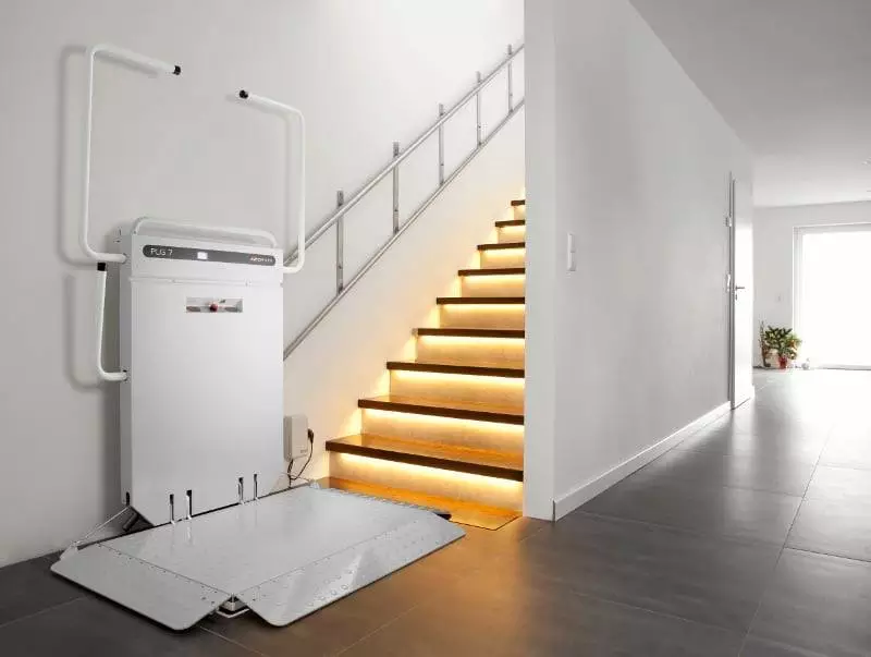 LSM Mobility Plateforme élévatrice blanche PLG 7 pour fauteuil roulant installée près d'un escalier moderne éclairé, dans un intérieur épuré. Solution d'accessibilité pour une maison colorée ou un décor discret.