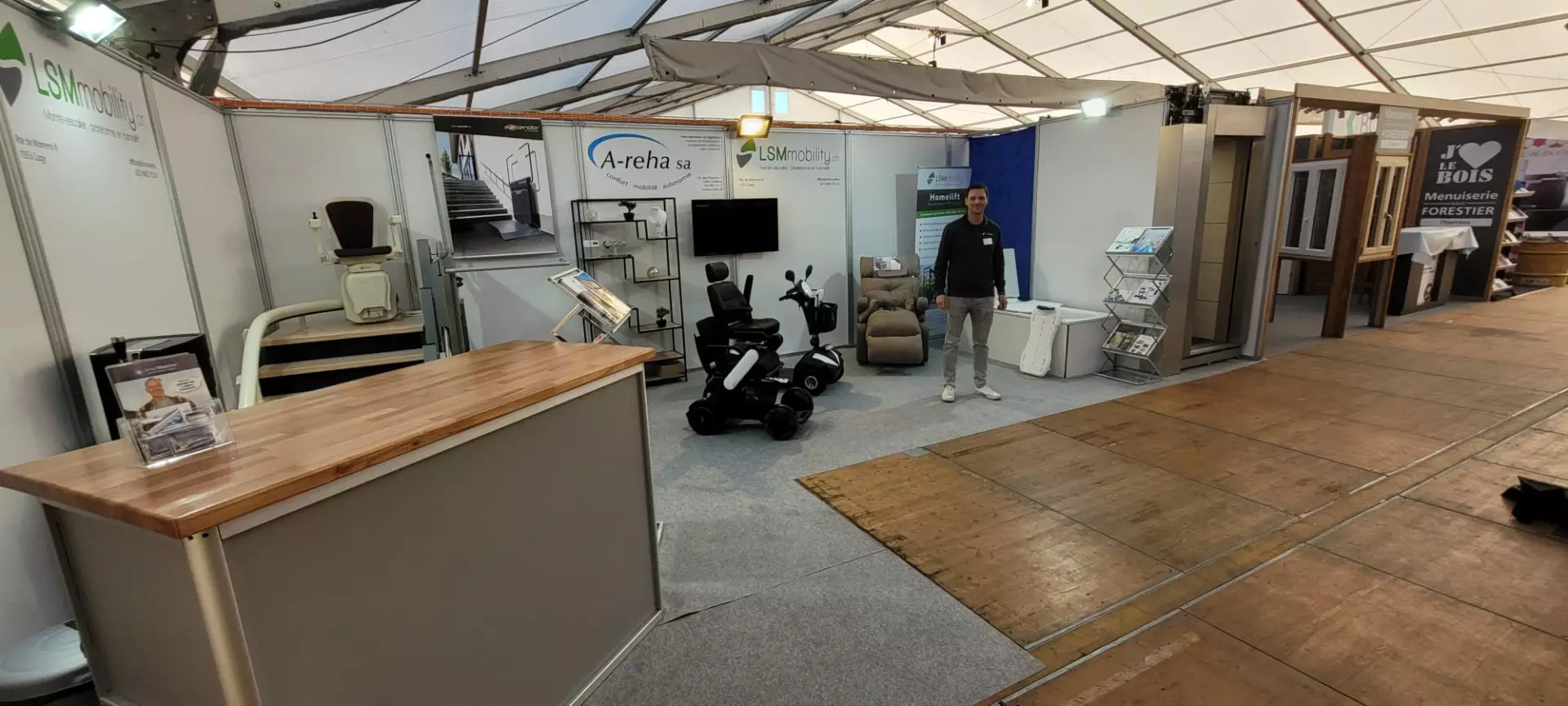 LSM Mobility Stand LSM Mobility à Interlift 2022, présentant des solutions d'accessibilité : monte-escaliers, scooters PMR, et ascenseurs privatifs. Un homme se tient devant un Homelift. Le stand met en avant le confort et l'autonomie.