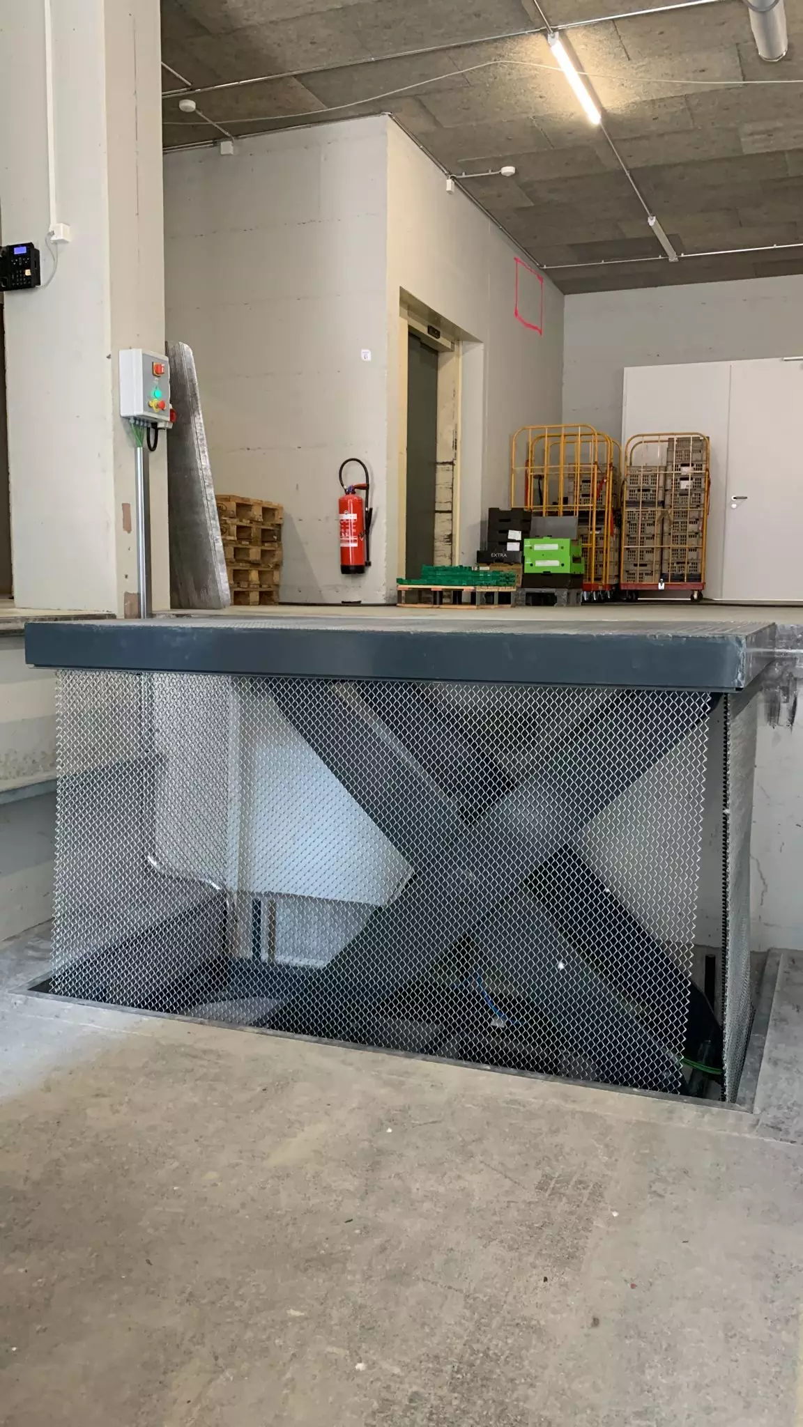 LSM Mobility Plateforme industrielle avec une barrière de sécurité grillagée, un extincteur rouge visible et des chariots de manutention en arrière-plan. Éclairage industriel typique.