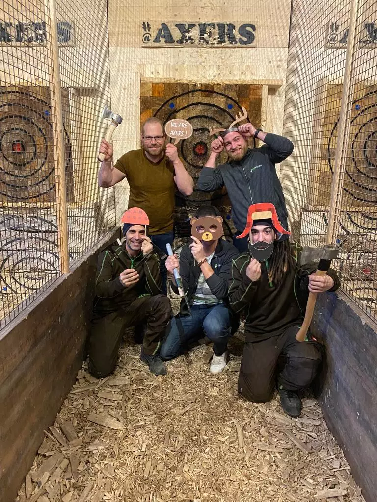 LSM Mobility Un groupe d'amis célèbrent les fêtes de fin d’année en faisant du lancer de haches. Ils portent des masques et posent joyeusement devant les cibles. #Axers
