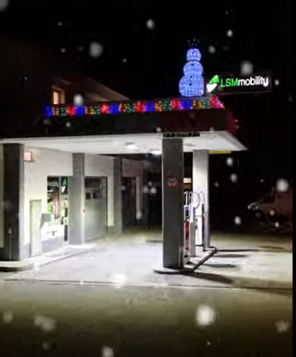 LSM Mobility Station-service décorée pour les fêtes de fin d'année avec des lumières colorées et un bonhomme de neige lumineux. LSMmobility est également visible. Ambiance festive et hivernale.
