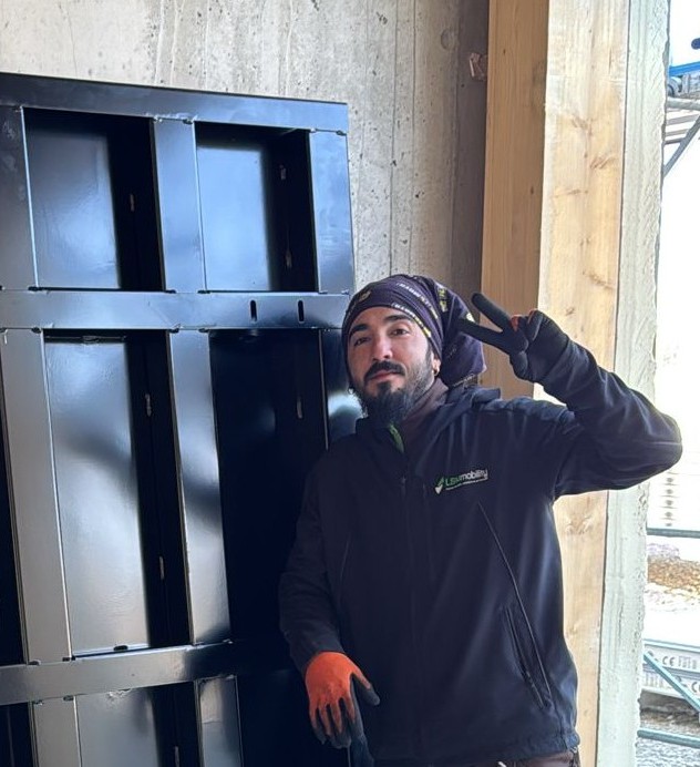 LSM Mobility Un employé de Lisamobility, souriant et faisant un signe de paix, se tient devant des modules noirs sur un chantier, prêt pour une "petite mise en jambe".