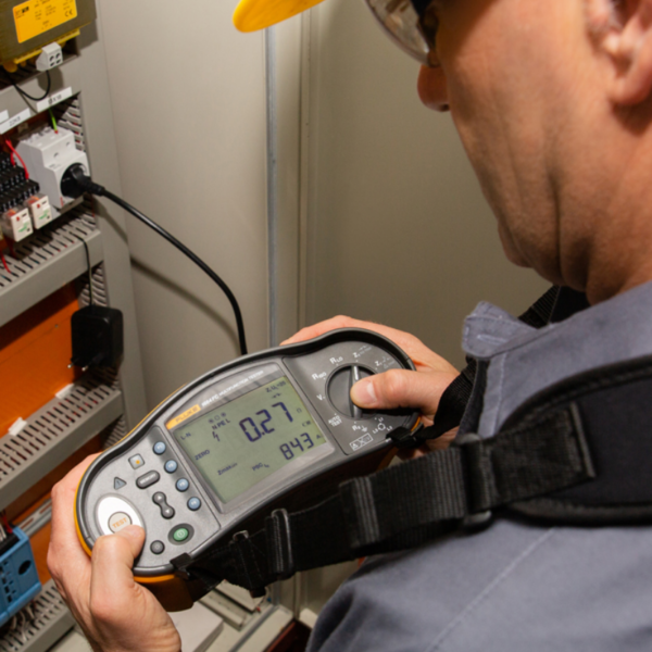 LSM Mobility Un électricien effectue un Contrôle OIBT avec un multimètre Fluke. L'appareil affiche "0.27". L'homme porte un casque jaune et des lunettes de sécurité.